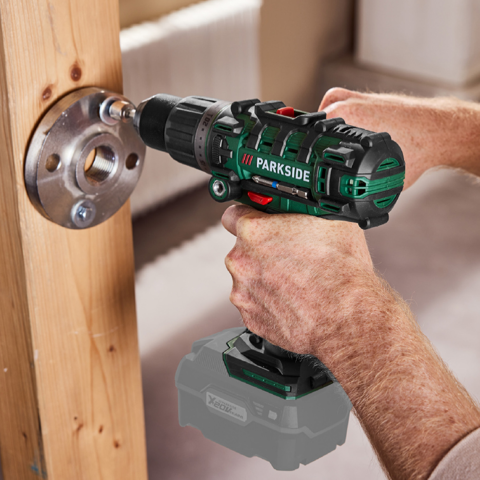 Un homme utilise une perceuse-visseuse sans fil pour visser une bride métallique sur une poutre en bois.