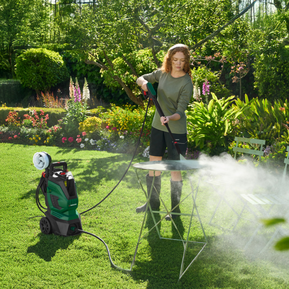 Femme nettoyant une table de jardin avec un nettoyeur haute pression dans un jardin fleuri.