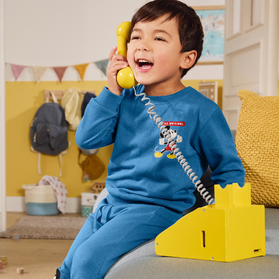 Enfant en pyjama bleu avec un motif de personnage de dessin animé, jouant avec un téléphone jaune.