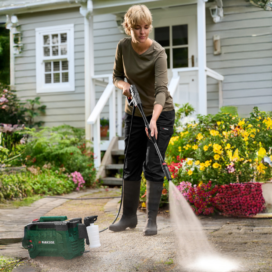Une femme nettoie une allée avec un nettoyeur haute pression et un pulvérisateur de détergent.