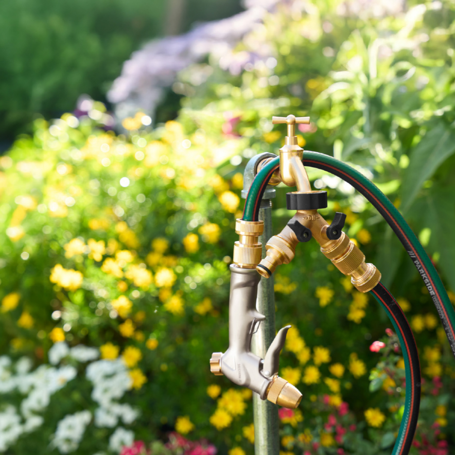 Robinet de jardin en laiton avec tuyau et pistolet d'arrosage, sur fond de fleurs.