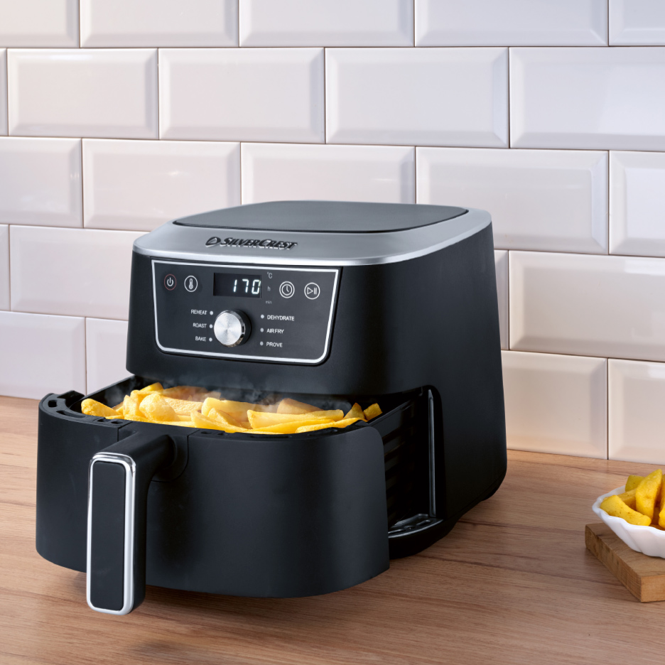 Friteuse à air chaud noire avec des frites dorées, sur un comptoir en bois.