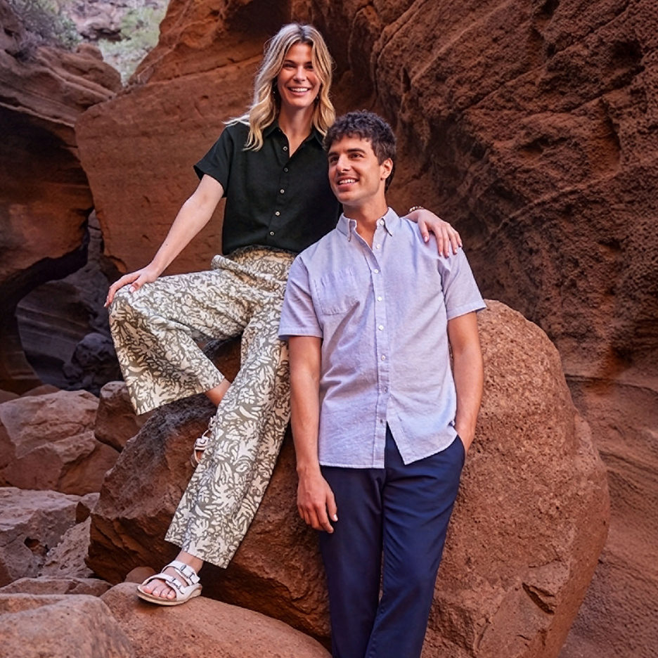 Un couple souriant en chemises et pantalons décontractés dans un canyon rocheux.