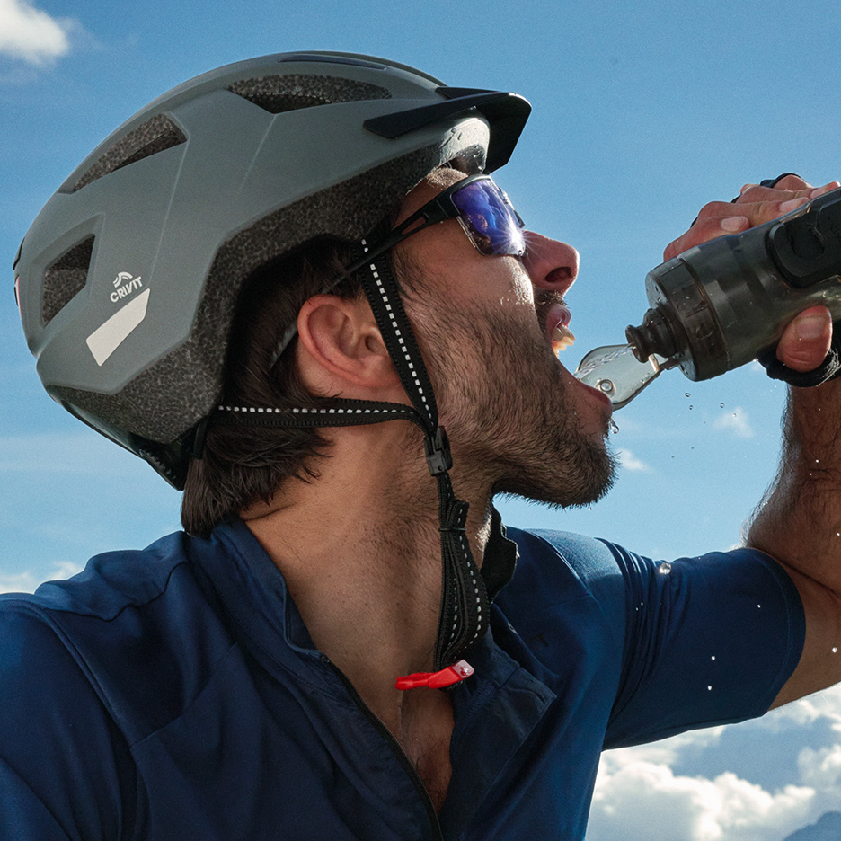 Cycliste avec casque et lunettes de soleil buvant de l'eau d'une gourde.