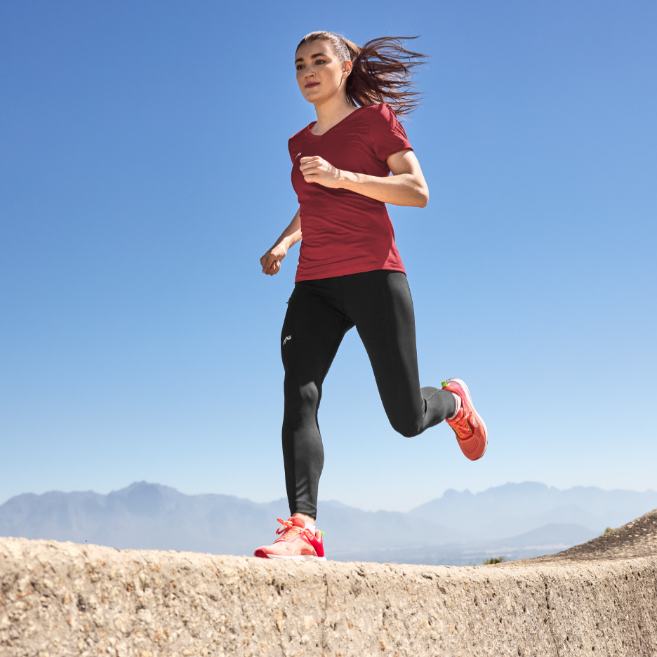 Femme en t-shirt de sport rouge et leggings noirs, courant en extérieur.