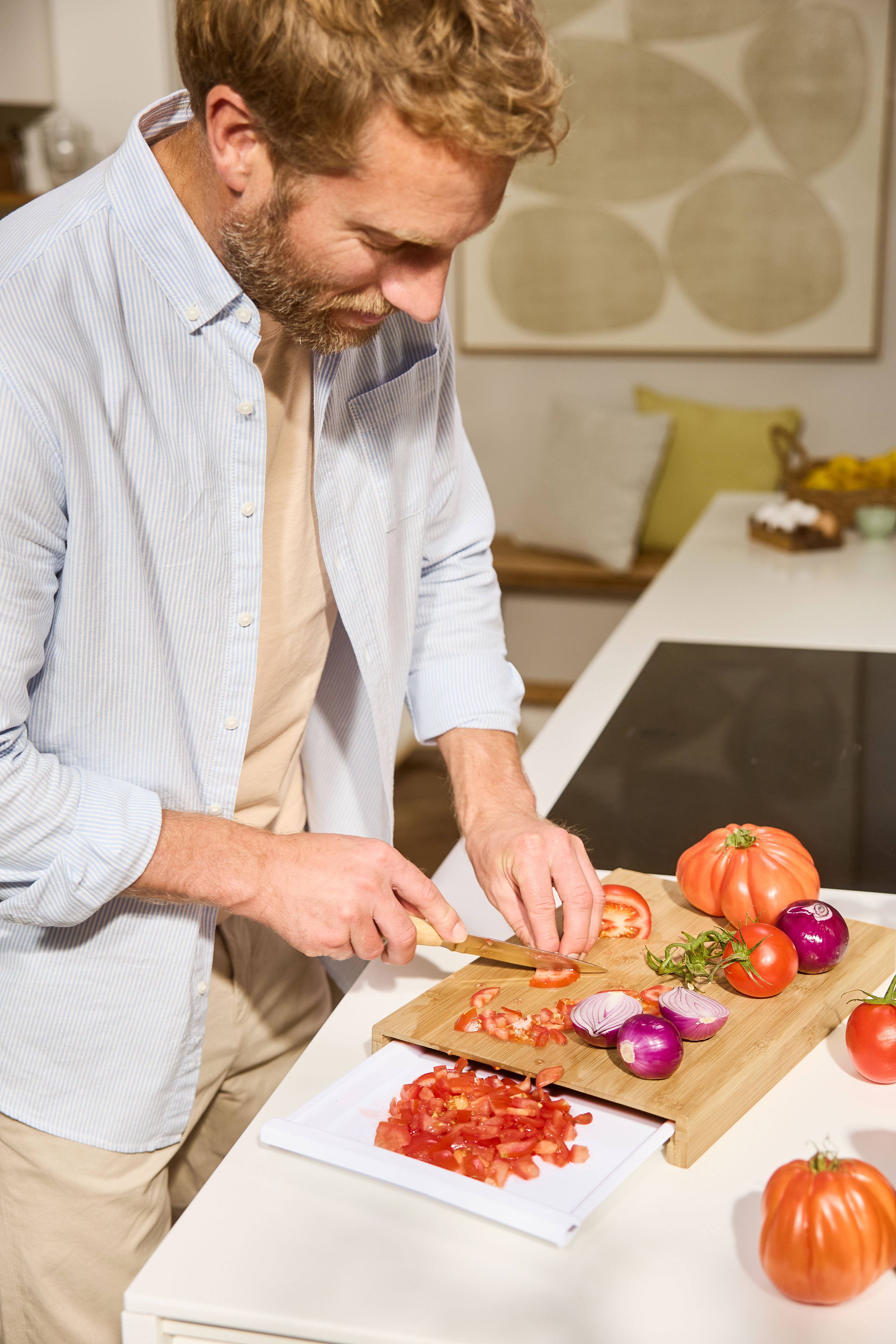 Homme coupant des tomates et des oignons sur une planche à découper en bois dans la cuisine.