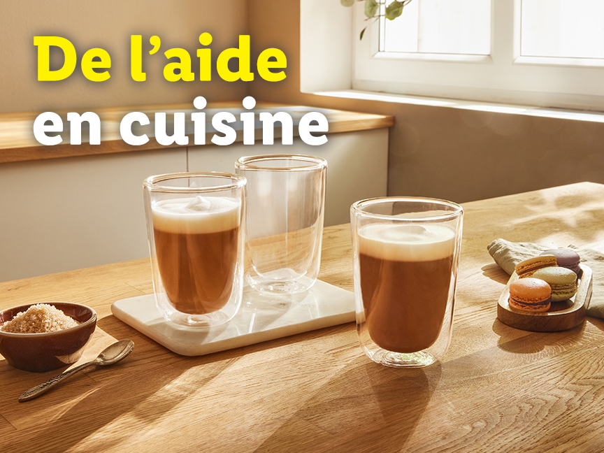 Trois verres à double paroi contenant un cappuccino sont posés sur une table en bois, à côté de macarons.