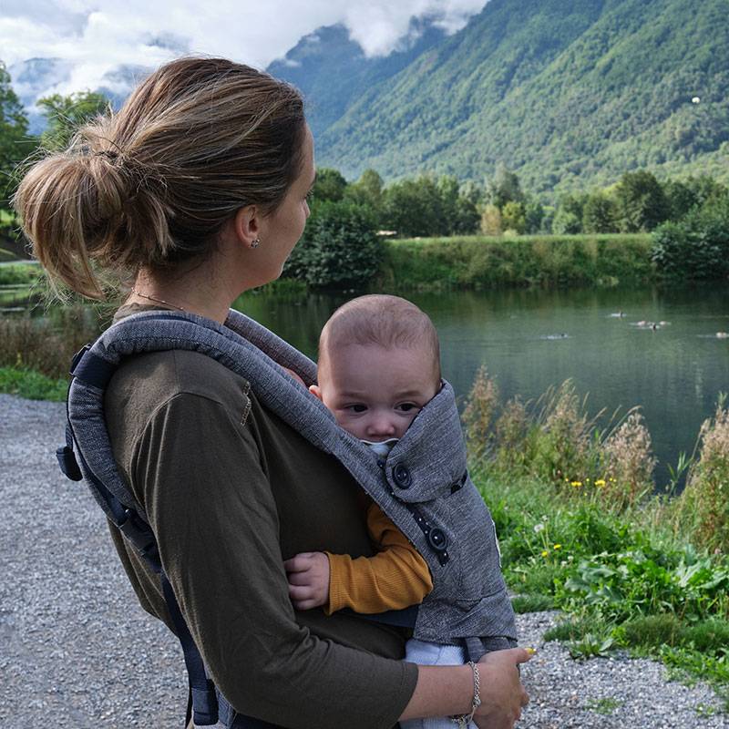 Mère avec bébé dans un porte-bébé dehors.