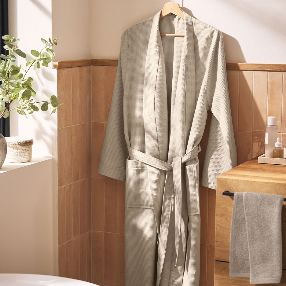 Peignoir gaufré beige suspendu dans une salle de bain avec carrelage marron et plantes.
