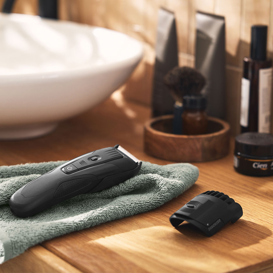 Tondeuse à cheveux noire sur une serviette verte dans une salle de bain avec lavabo et produits.