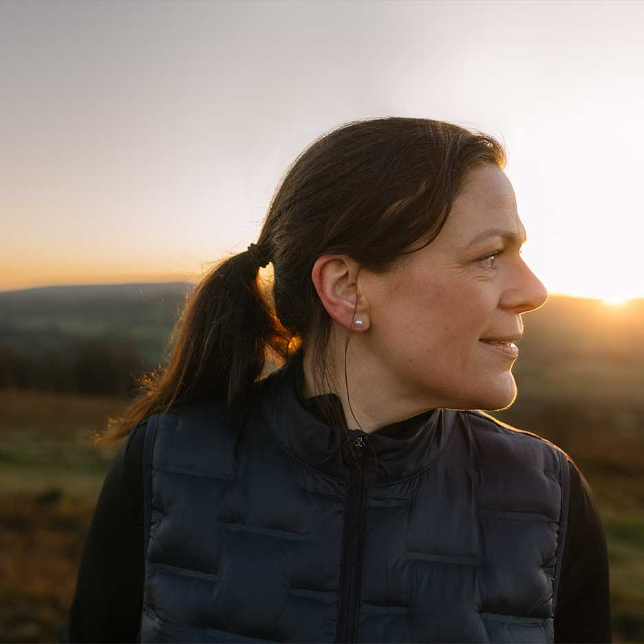 Femme en gilet noir et pull noir au coucher du soleil.