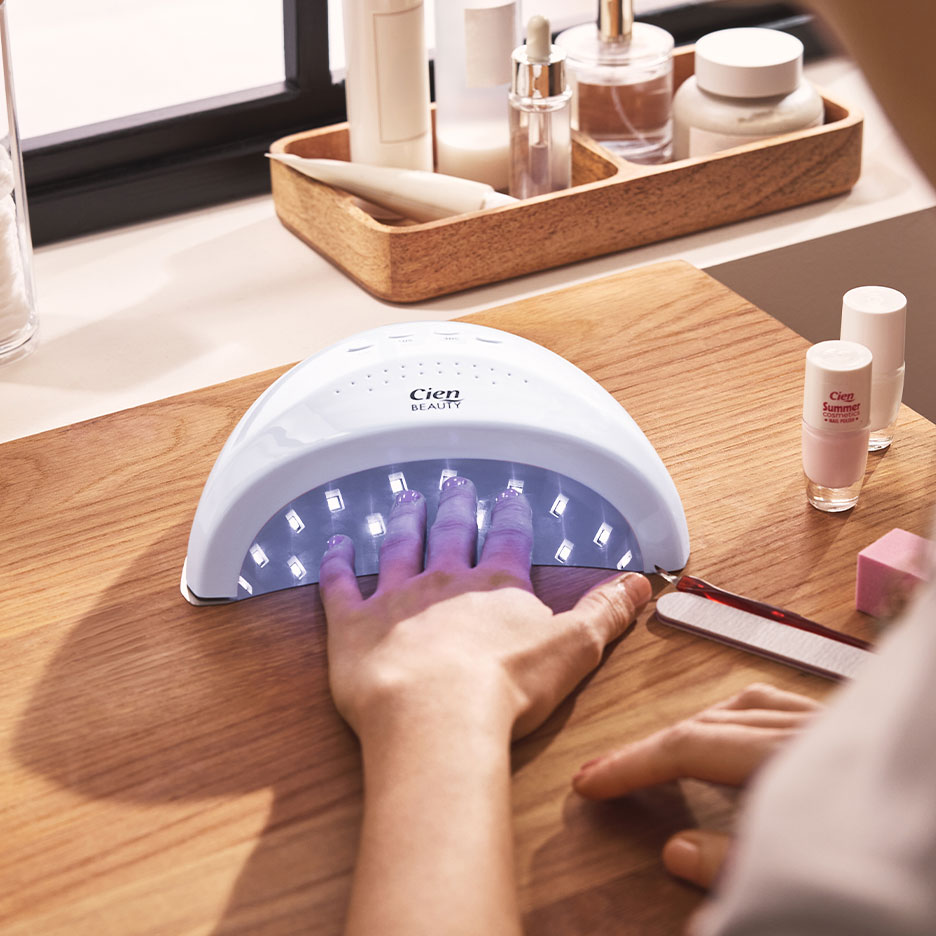 Femme séchant ses ongles sous une lampe UV, avec vernis et accessoires de manucure.