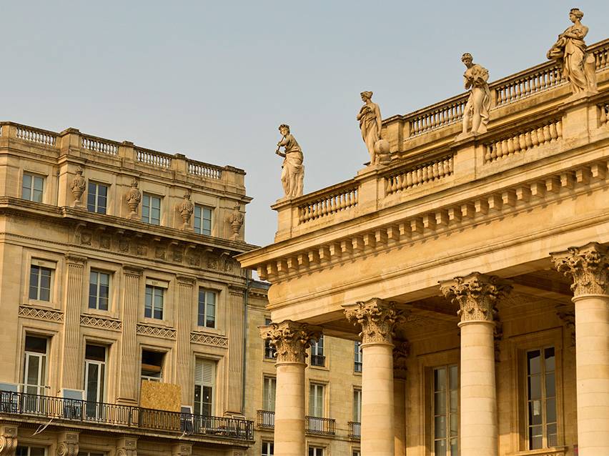 Façade de bâtiment historique avec des statues sur le toit et des colonnes corinthiennes.