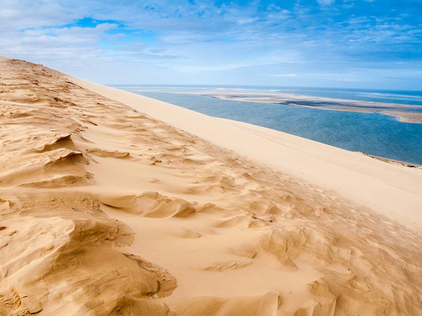 Dune de sable doré avec un lagon bleu et un ciel nuageux en arrière-plan.