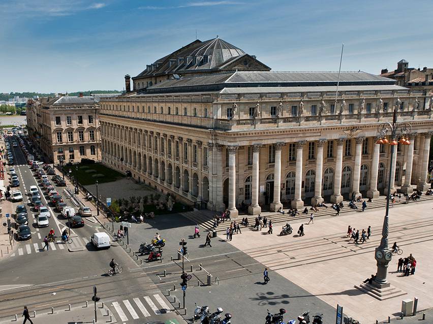 Vue aérienne du Grand Théâtre de Bordeaux avec des personnes et des voitures dans la rue.