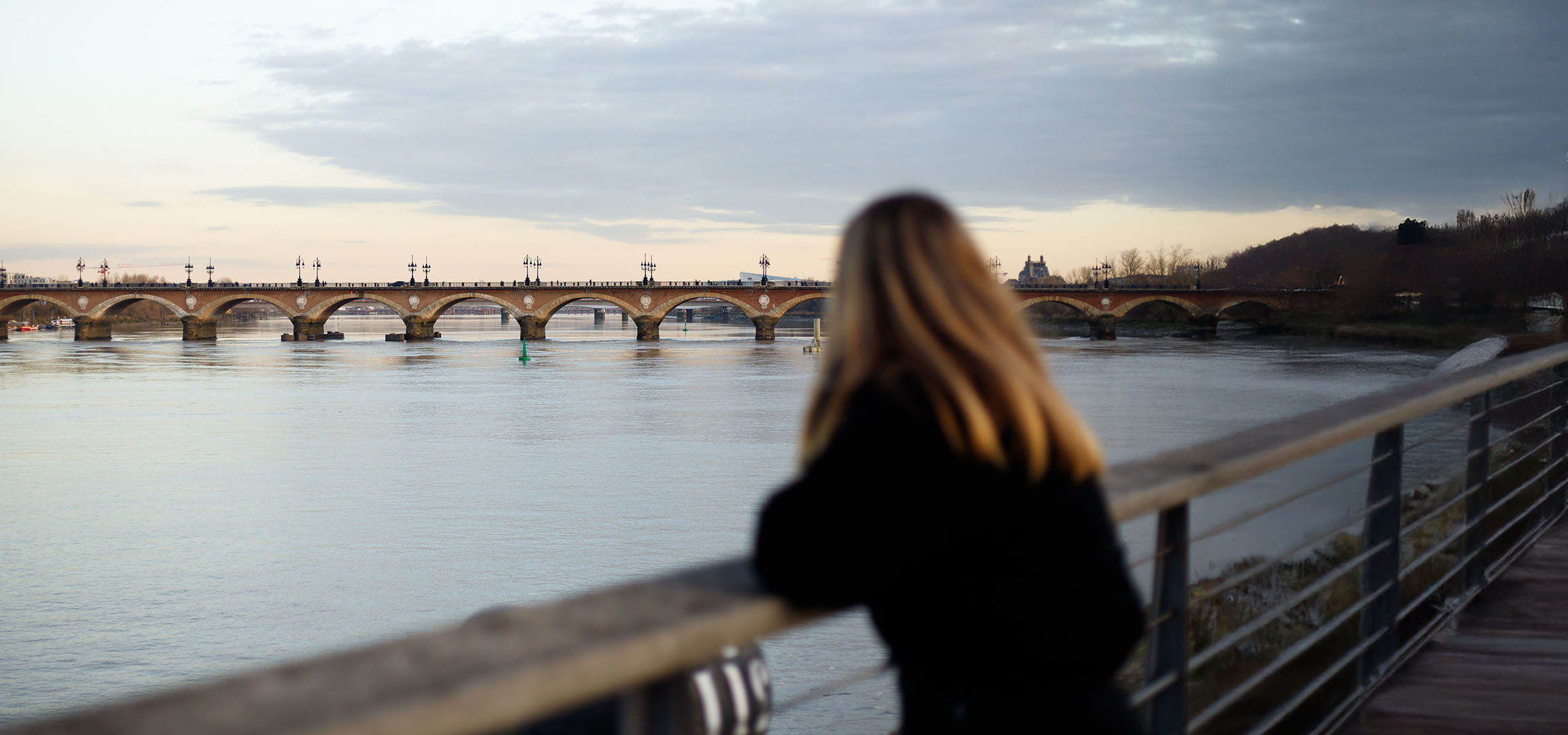Vue d'un pont à arches et d'une rivière, avec une personne aux cheveux longs de dos.