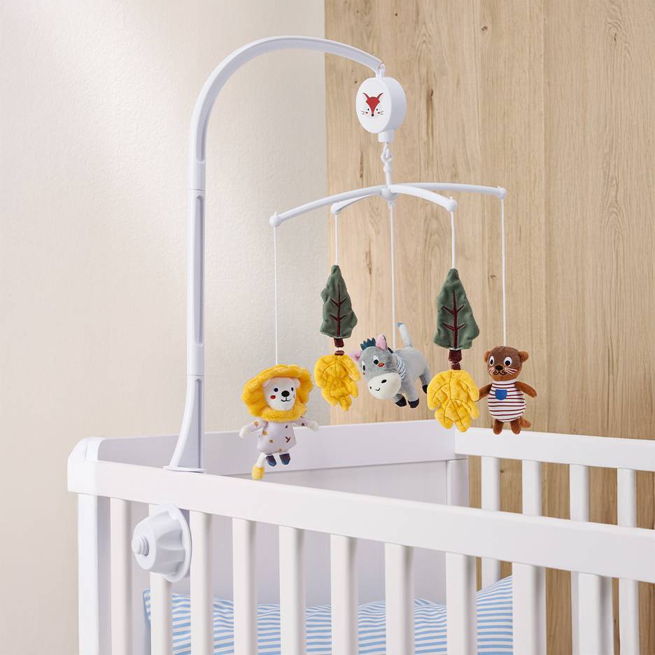 Lit bébé blanc avec un mobile d'animaux et d'arbres en jouets.