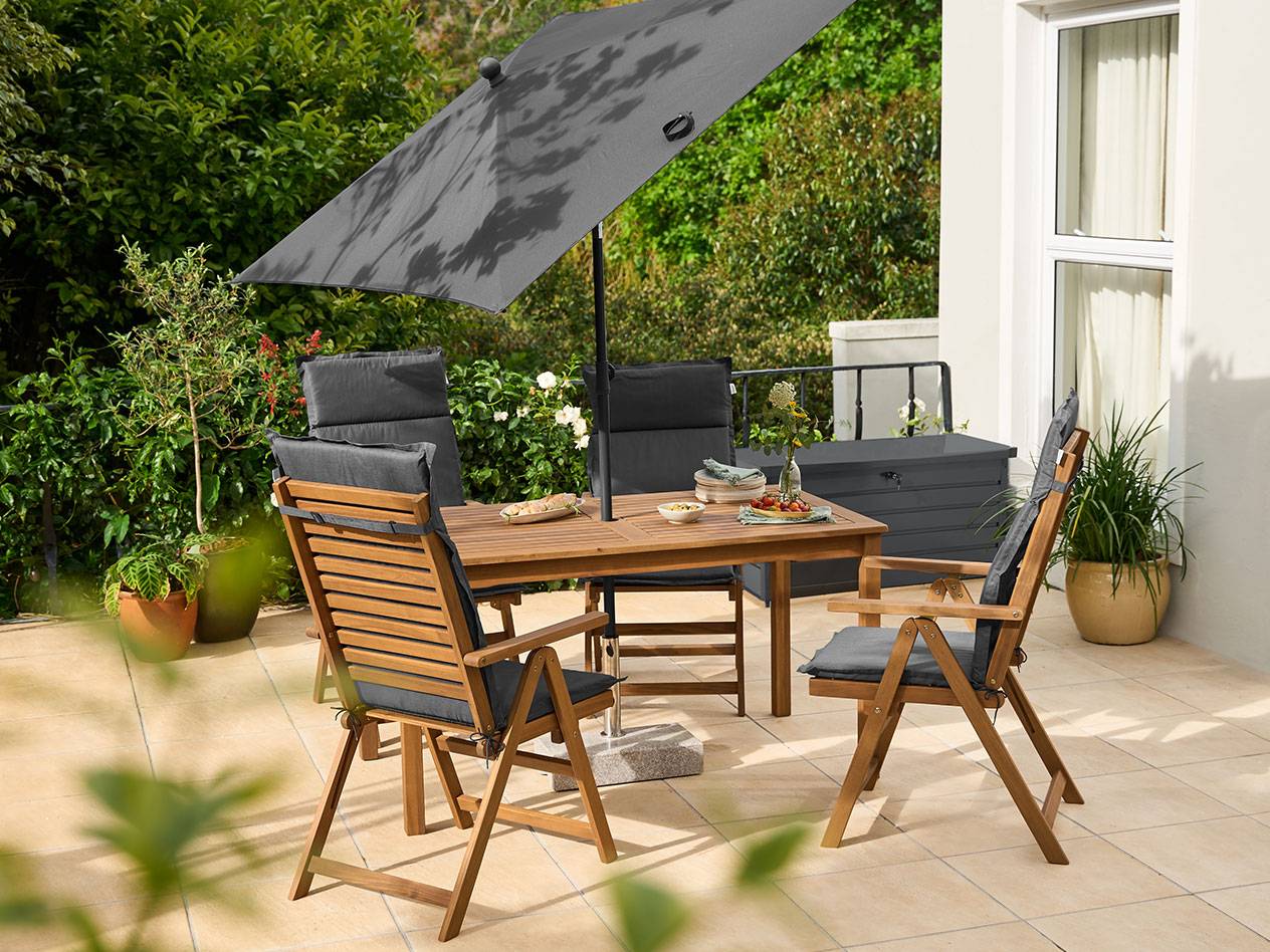Ensemble de salle à manger de jardin en bois avec coussins gris et grand parasol gris sur une terrasse.