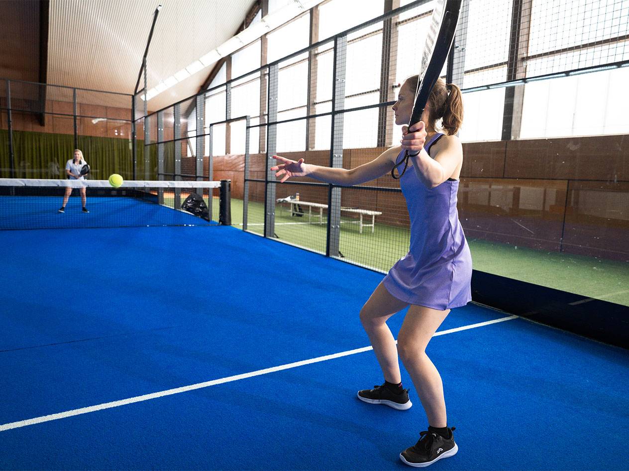 Femme en robe violette jouant au padel sur un court bleu.