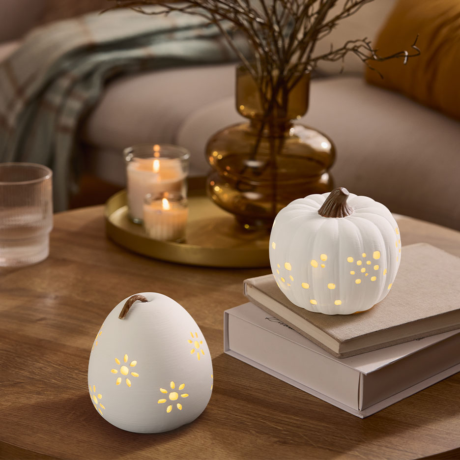 Deux citrouilles décoratives blanches illuminées sur une table en bois avec des bougies et un vase.