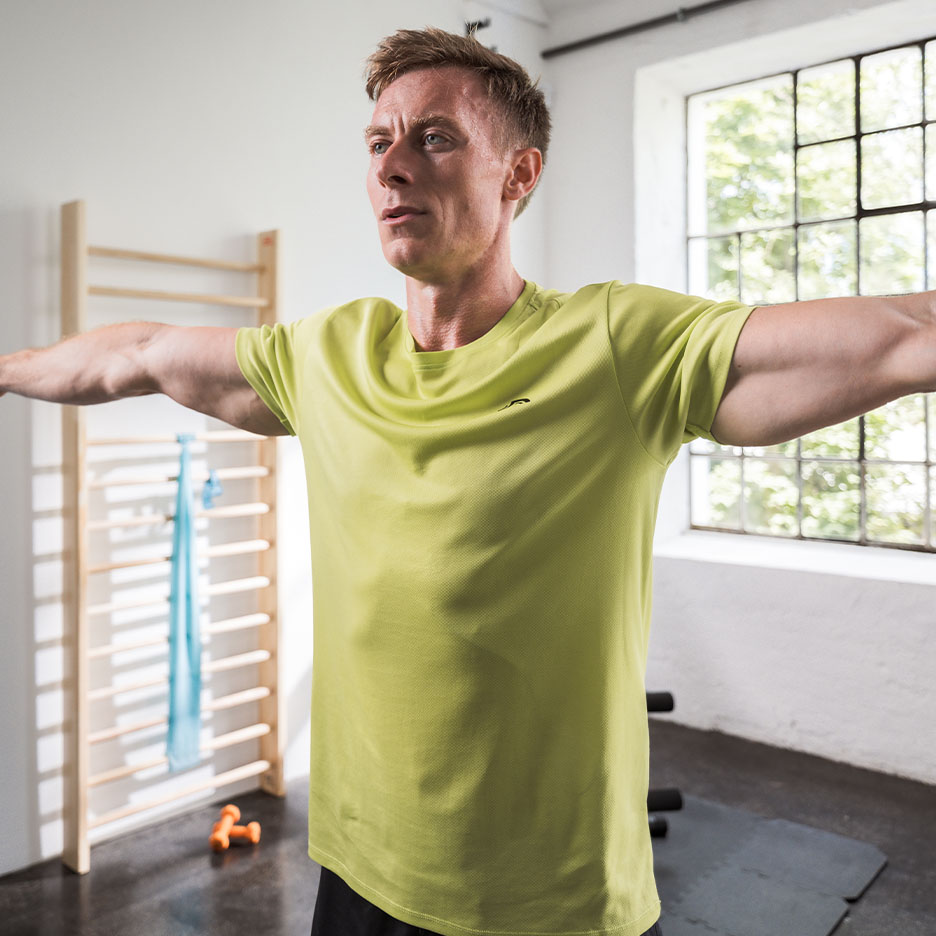 Homme en t-shirt de sport vert s'entraînant dans une salle de sport.