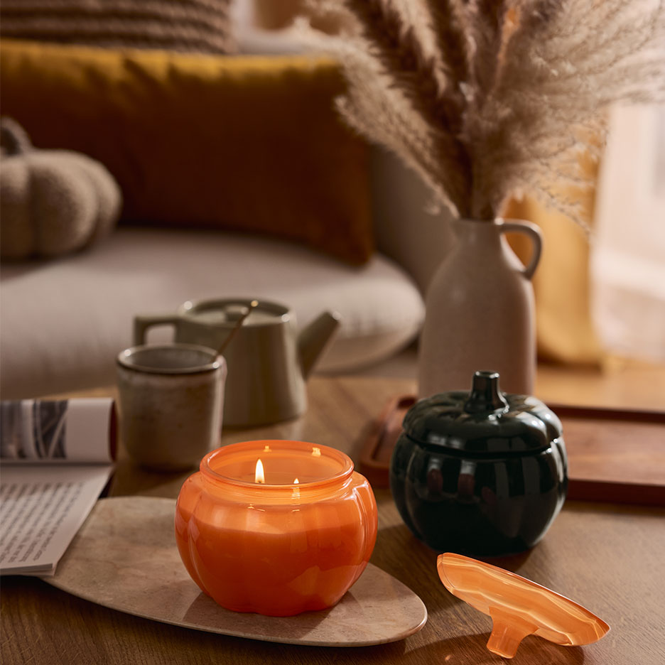 Bougie et récipient en forme de citrouille sur une table basse avec décor d'automne.