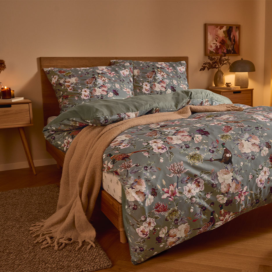 Lit en bois avec parure de lit florale verte et couverture marron.