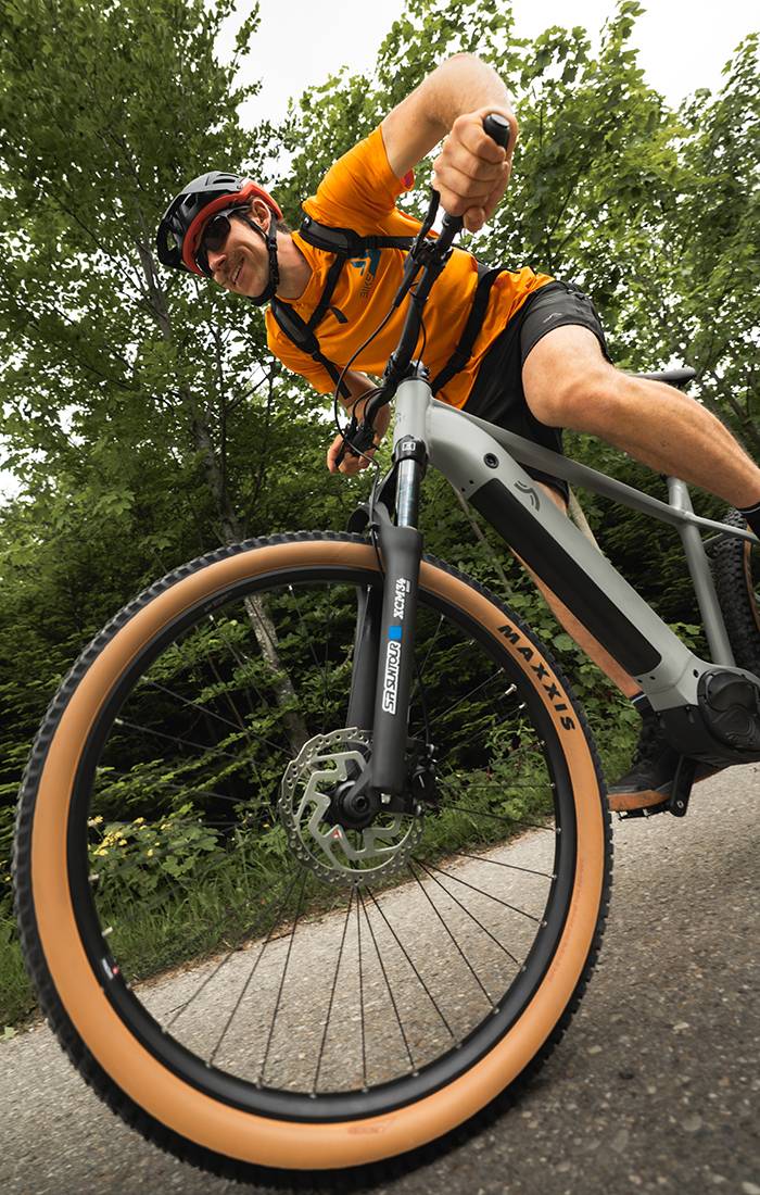 Un homme roule à vélo électrique Maxxis gris dans une forêt.