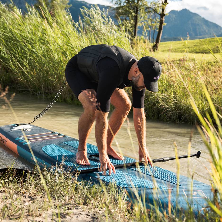Homme en combinaison et gilet de sauvetage se préparant pour le stand-up paddle sur une rivière.