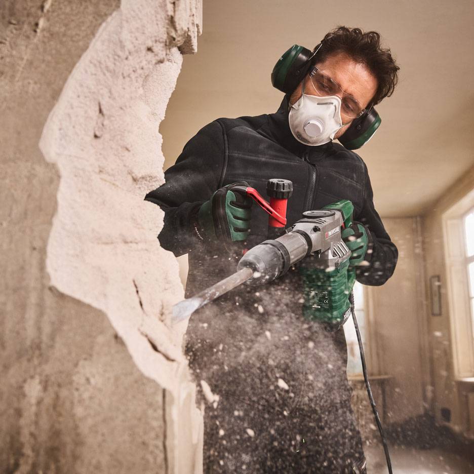 Homme avec marteau-piqueur et équipement de protection démolissant un mur.
