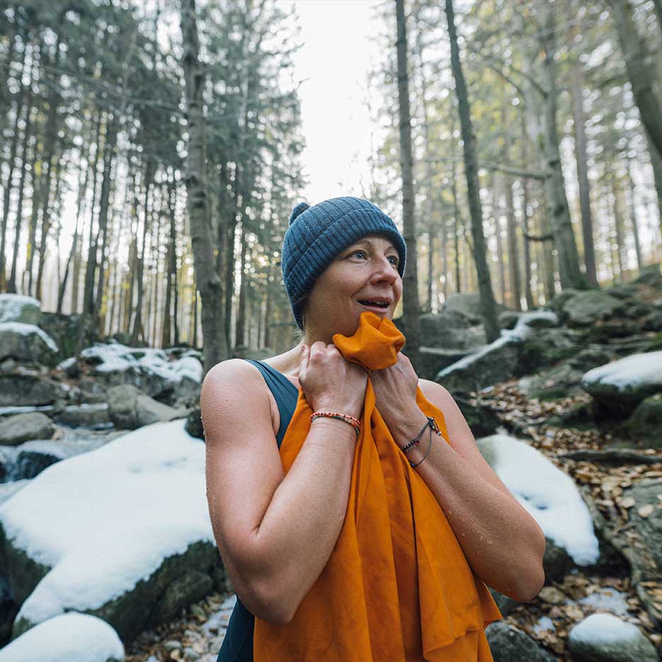 Femme en bonnet et maillot de bain se réchauffant avec une serviette dans une forêt enneigée.