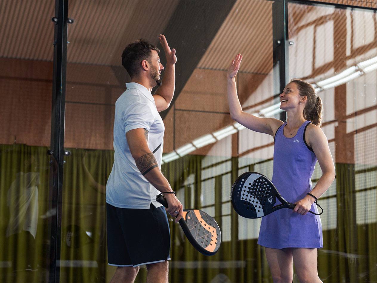 Deux joueurs de padel, un homme et une femme, se tapent dans la main sur le terrain.