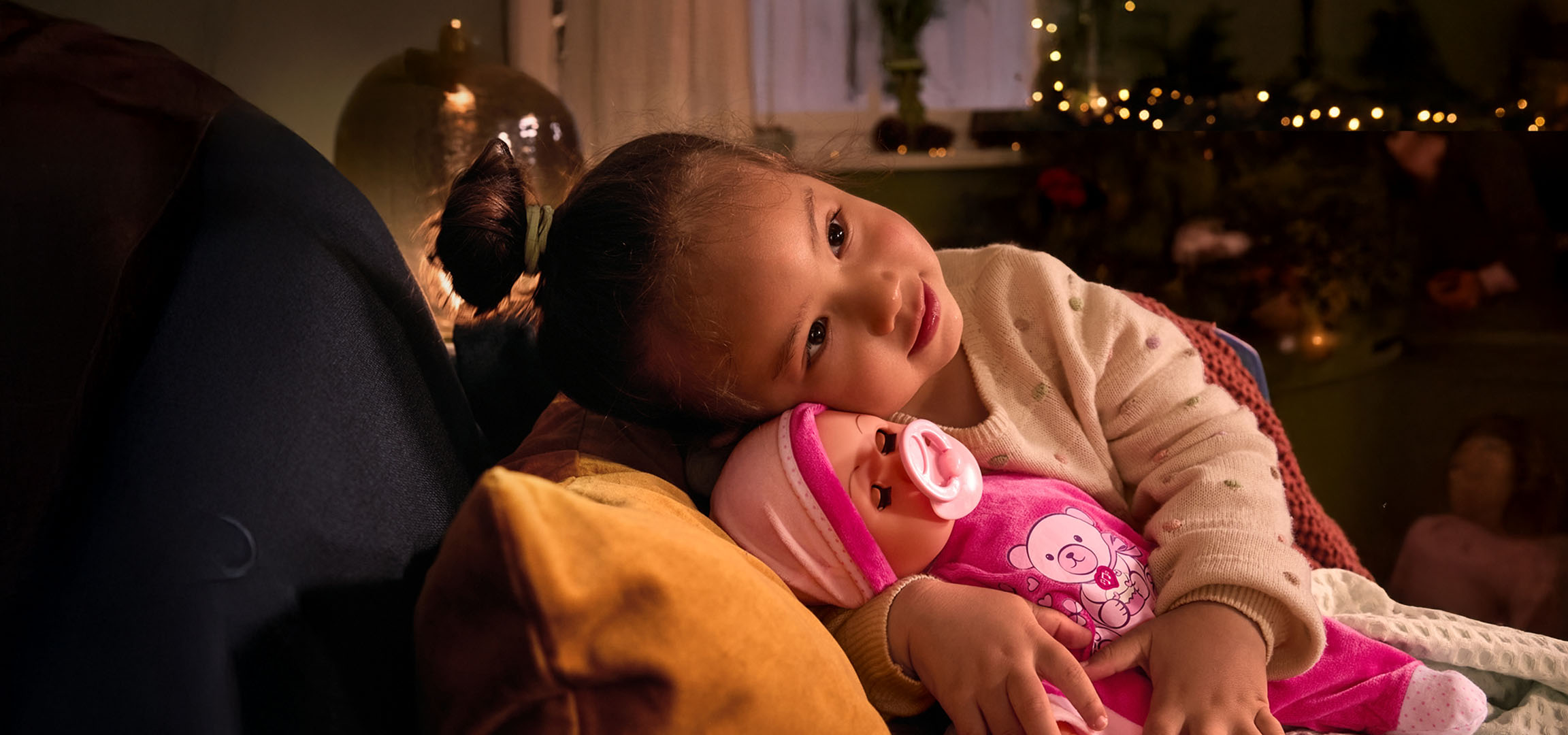 Fillette avec poupée et tétine, confortablement installée sur un coussin.