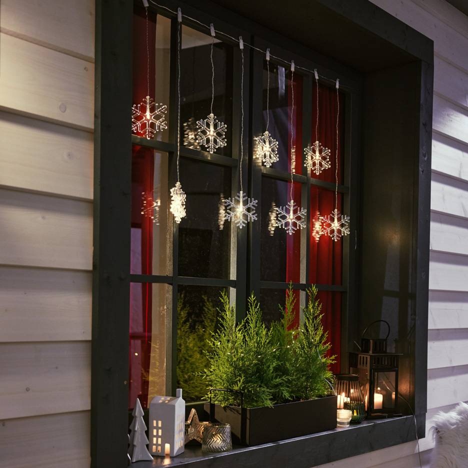Guirlande lumineuse flocon de neige dans une fenêtre avec petits sapins et bougies.