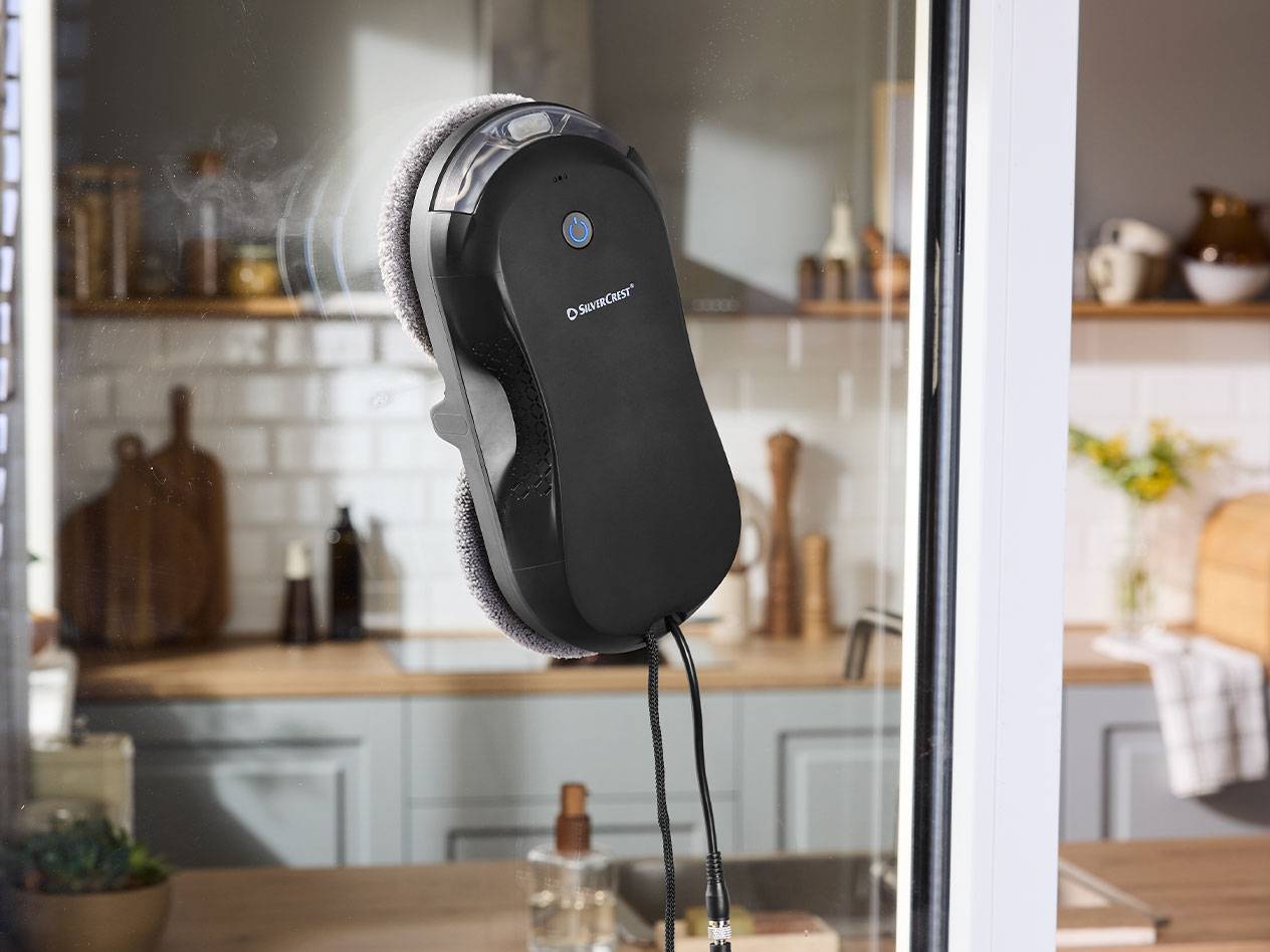 Robot lave-vitres Silvercrest sur une fenêtre avec une cuisine en arrière-plan.