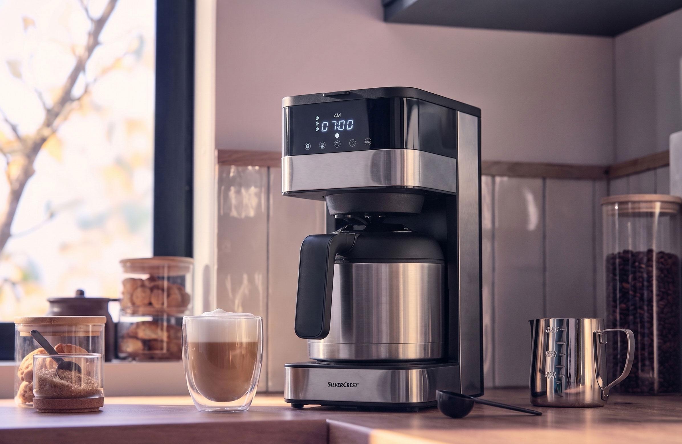 Cafetière avec verseuse isotherme et affichage numérique indiquant 07:00 AM, avec une tasse de café latte.