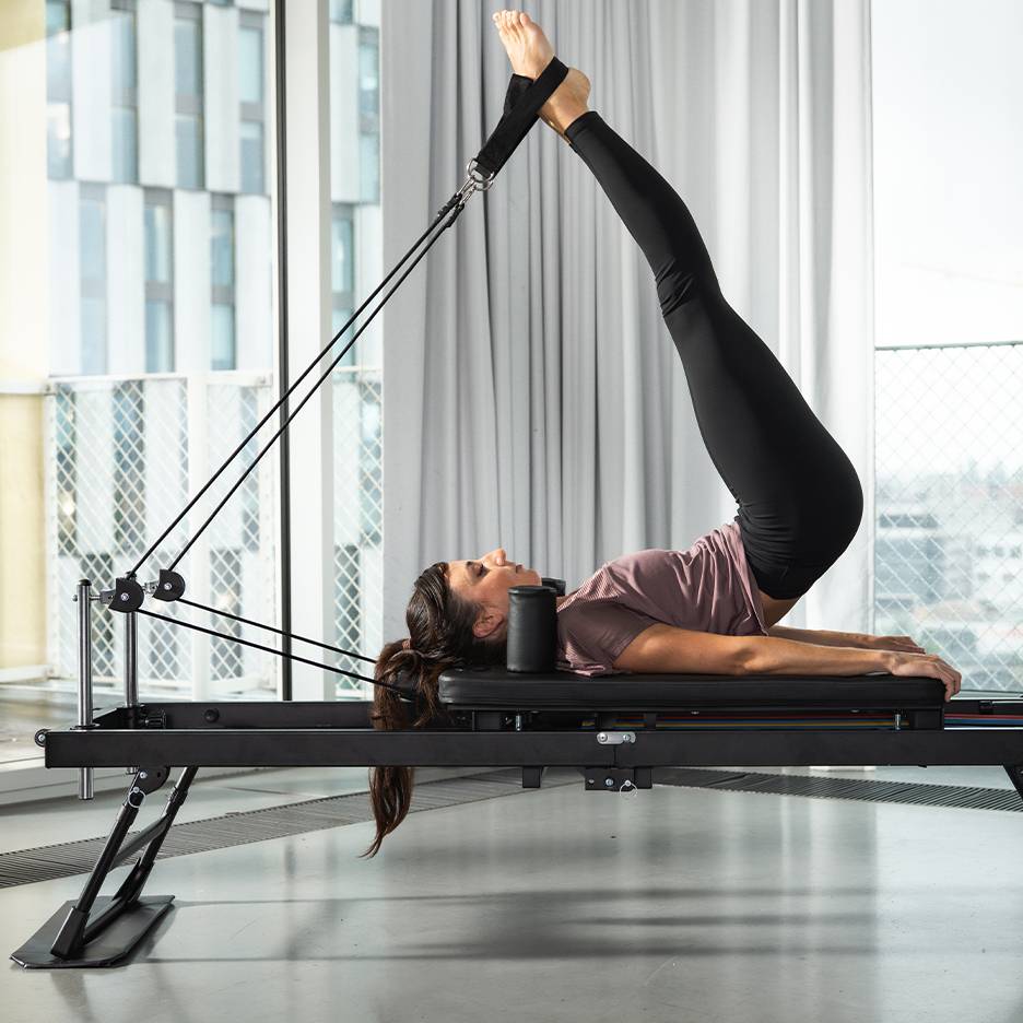 Femme faisant du Pilates sur un appareil noir, jambes levées.