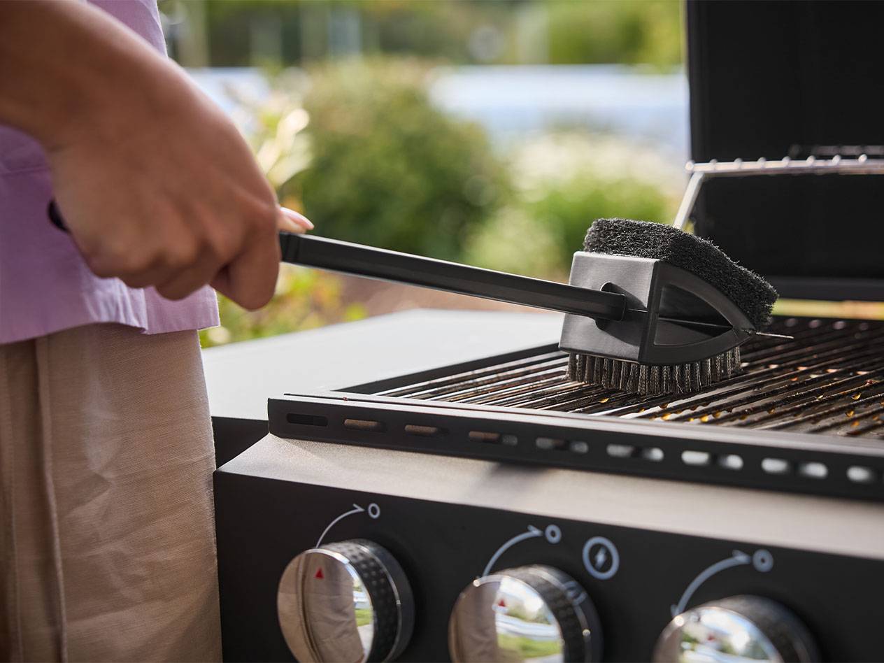 Personne nettoyant un barbecue avec une brosse à long manche.