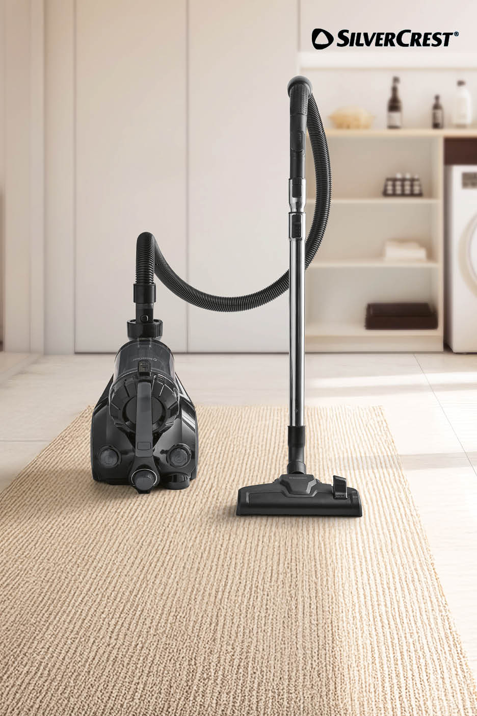 Aspirateur traîneau sans sac noir posé sur un tapis beige.