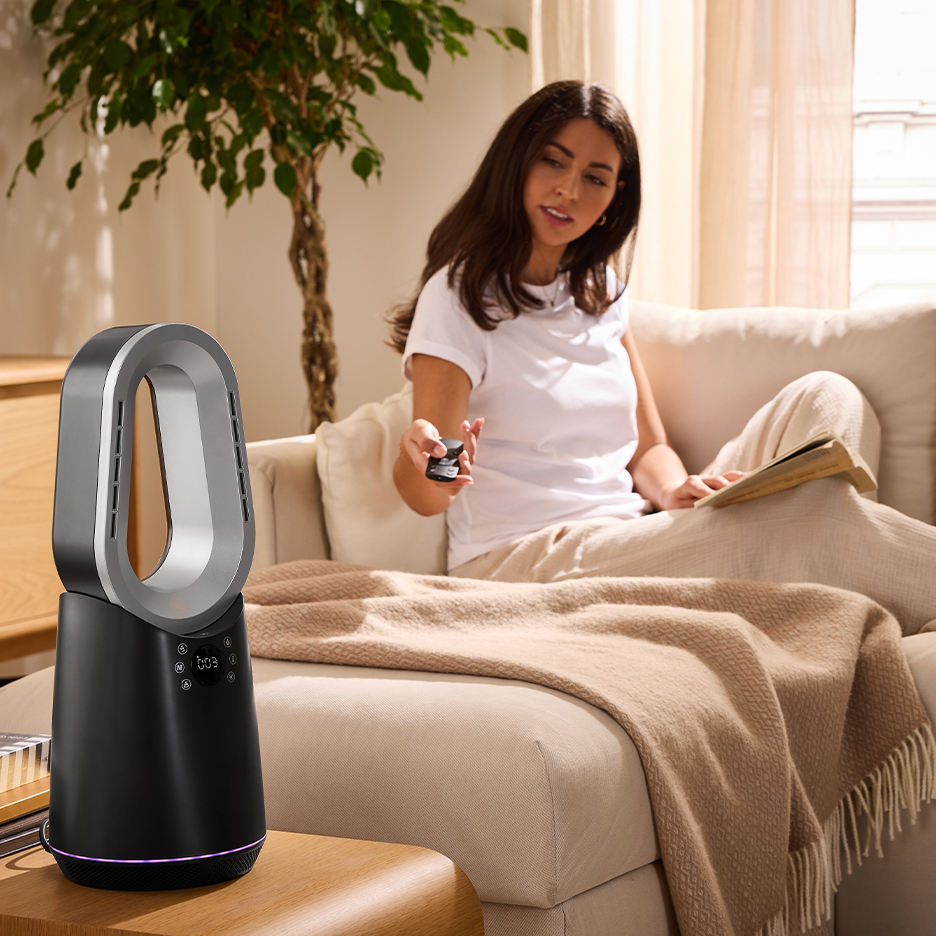Une femme sur un canapé utilise une télécommande pour contrôler un ventilateur sans pales noir et argenté.