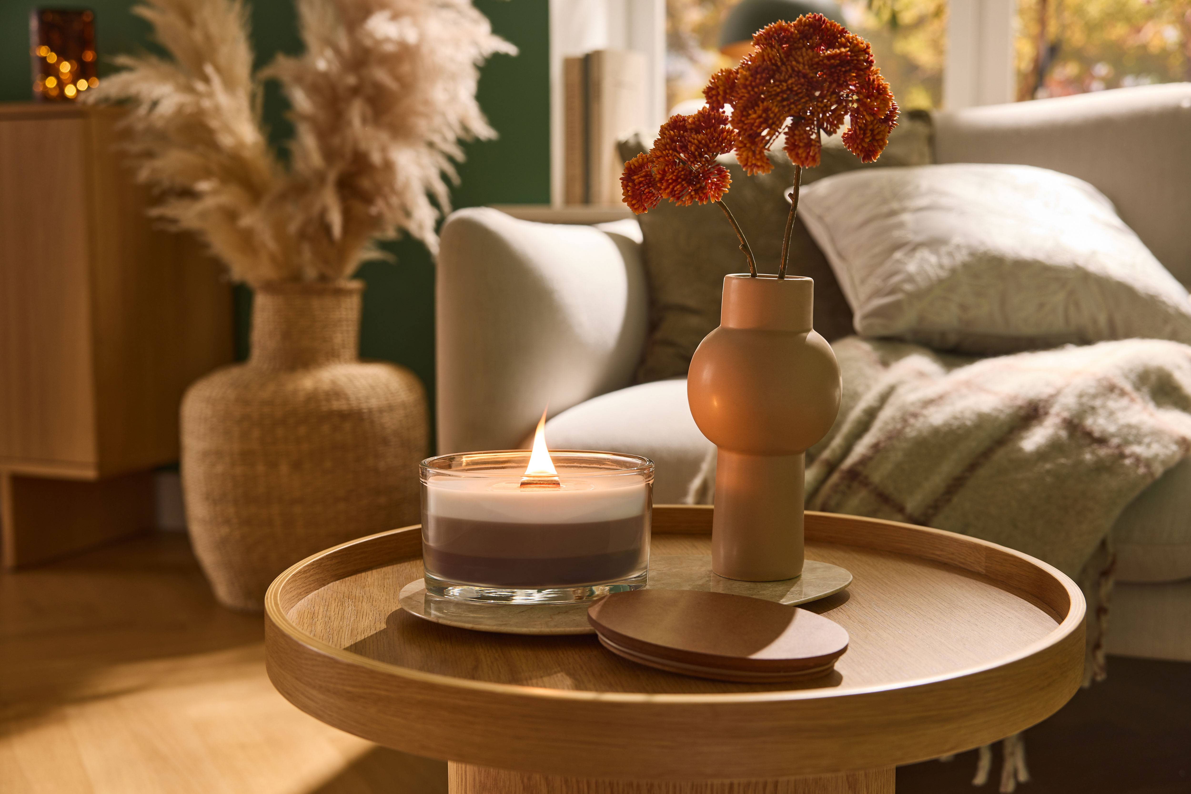Bougie allumée et vase de fleurs sur une table basse en bois dans un salon.