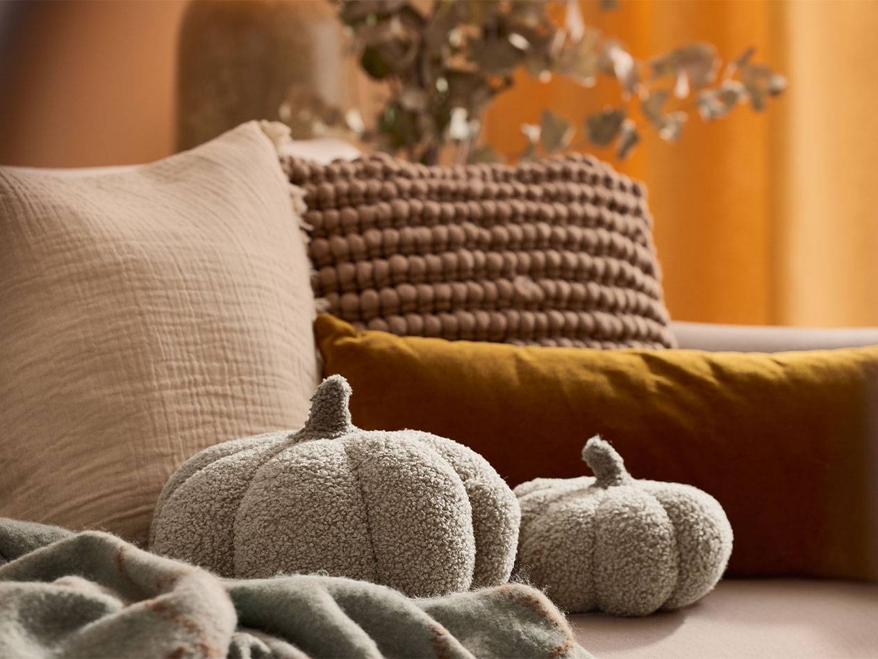 Deux citrouilles décoratives en peluche et des coussins aux tons terreux sur un canapé.