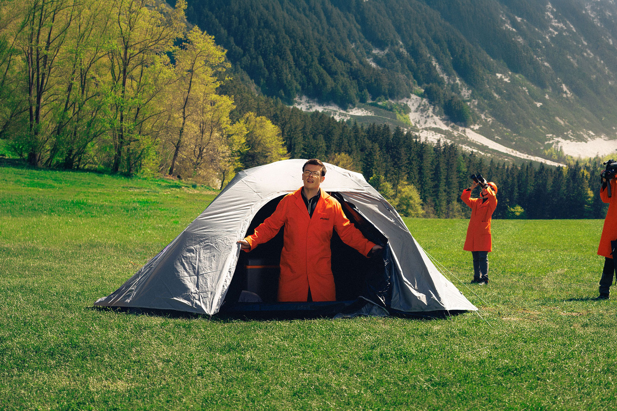 Généré par IA: Trois personnes en blouses oranges avec équipement de camping et d'observation dans une prairie.