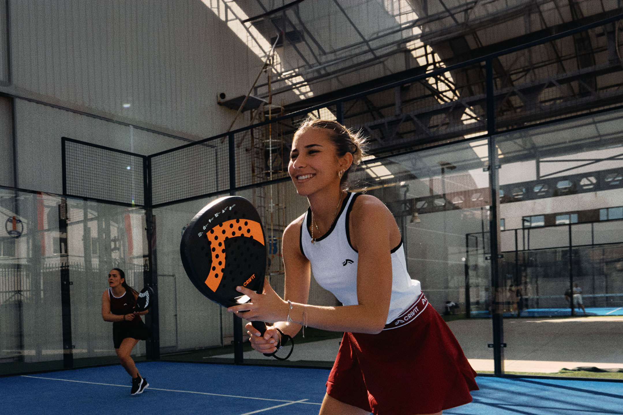 Généré par IA: Deux femmes jouant au padel, l'une souriante et tenant une raquette, sur un court bleu.