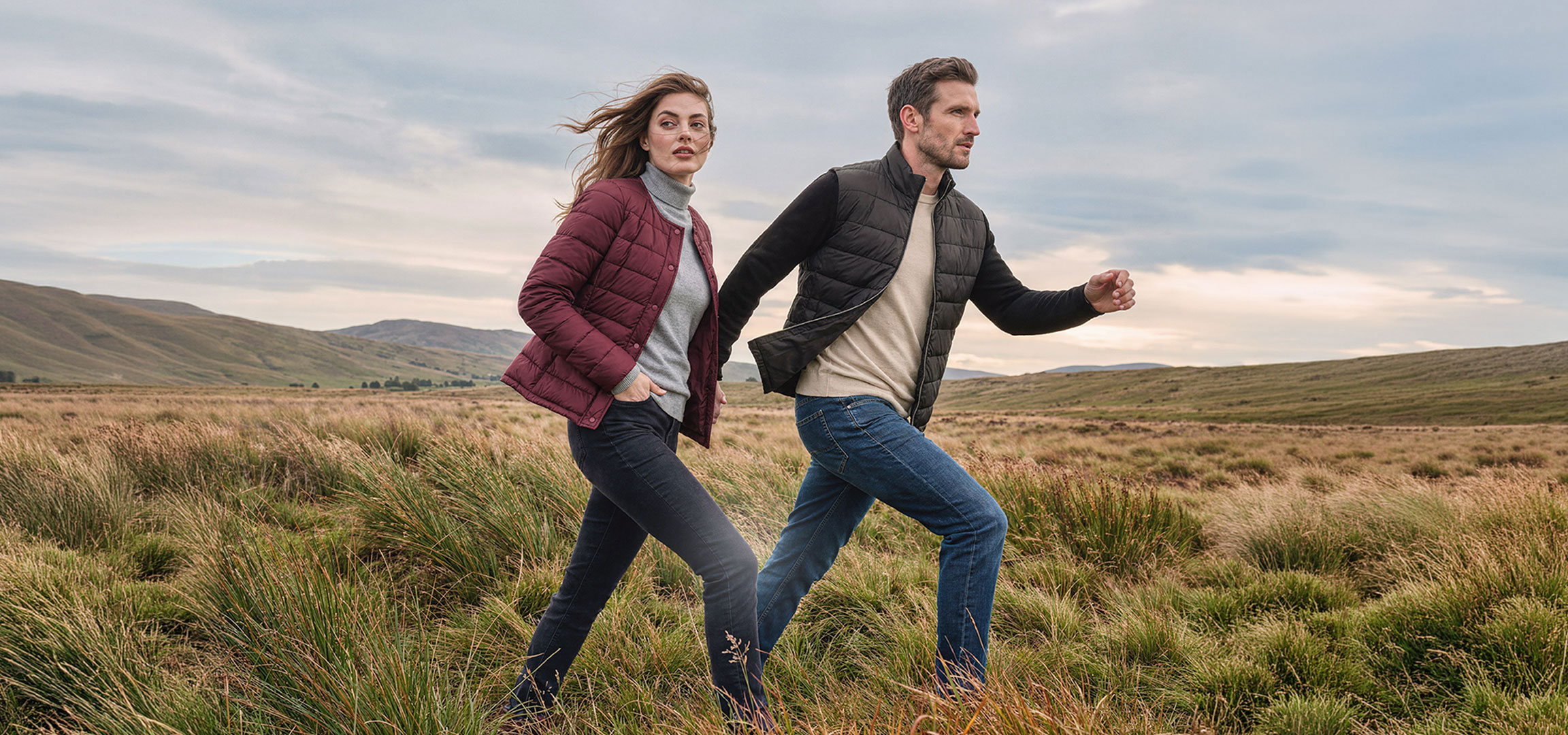 Généré par IA: Couple en doudounes légères et jeans marche dans un paysage vallonné et herbeux.