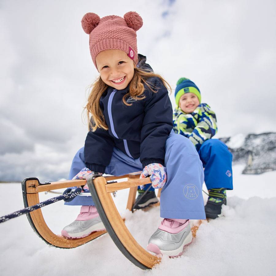 Enfants en vêtements d'hiver et bonnets à pompons, faisant de la luge dans la neige.