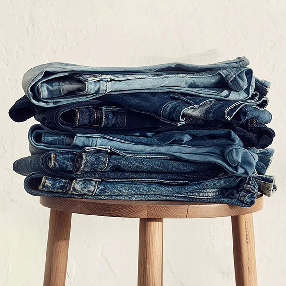 Pile de jeans de différentes nuances de bleu sur un tabouret en bois.