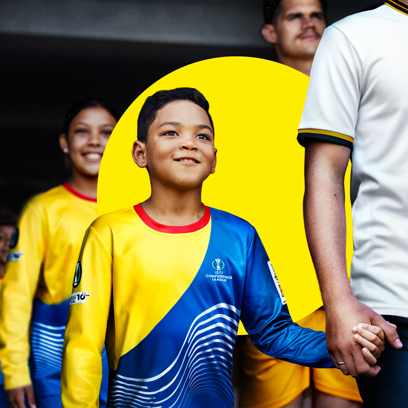 Un jeune garçon en maillot de football jaune et bleu tient la main d'un adulte.