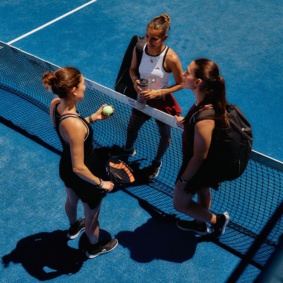 Agostina Bigotti et deux coéquipières en tenue de sport CRIVIT se tiennent ensemble près du filet de padel sur un court bleu après le match.
