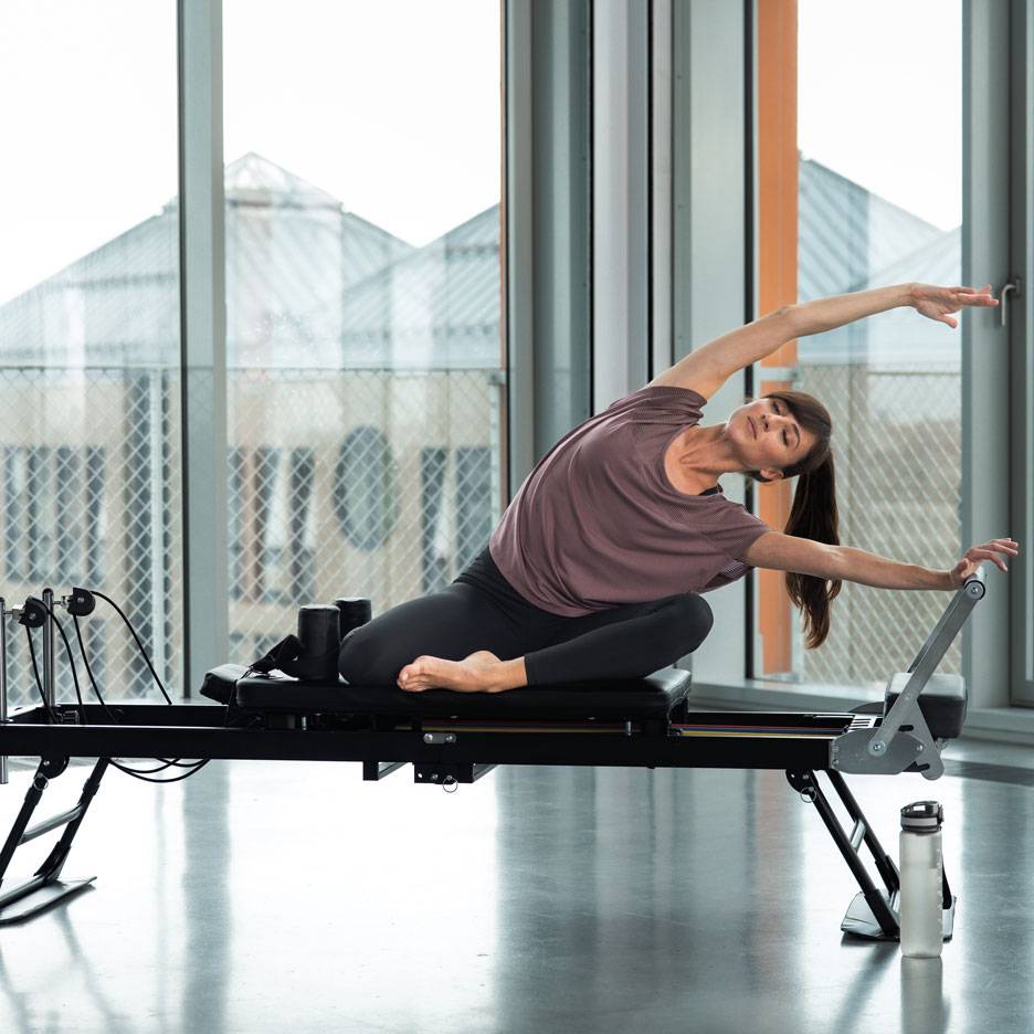 Femme faisant du Pilates sur un appareil reformer, s'étirant latéralement.